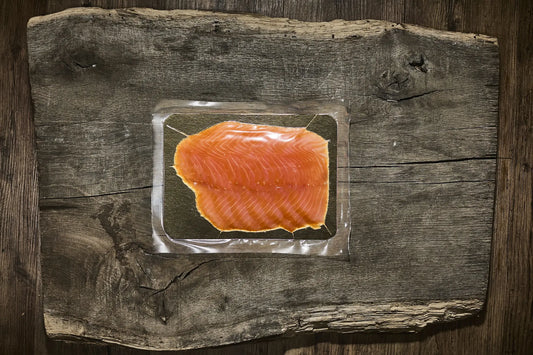 200 g Verpackung vom Räucherlachs auf einer golden platte. Lachs liegt auf einem brauen Holzbrett
