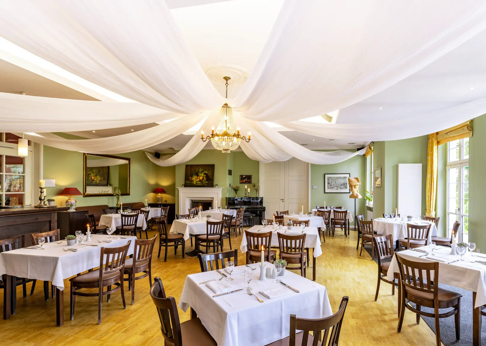 eine Saale mit Tischen und Stühlen im Restaurante. Eine frühlingshafte und fröhliche Stimmming. In der Mitte hängt ein Kronleuchter 